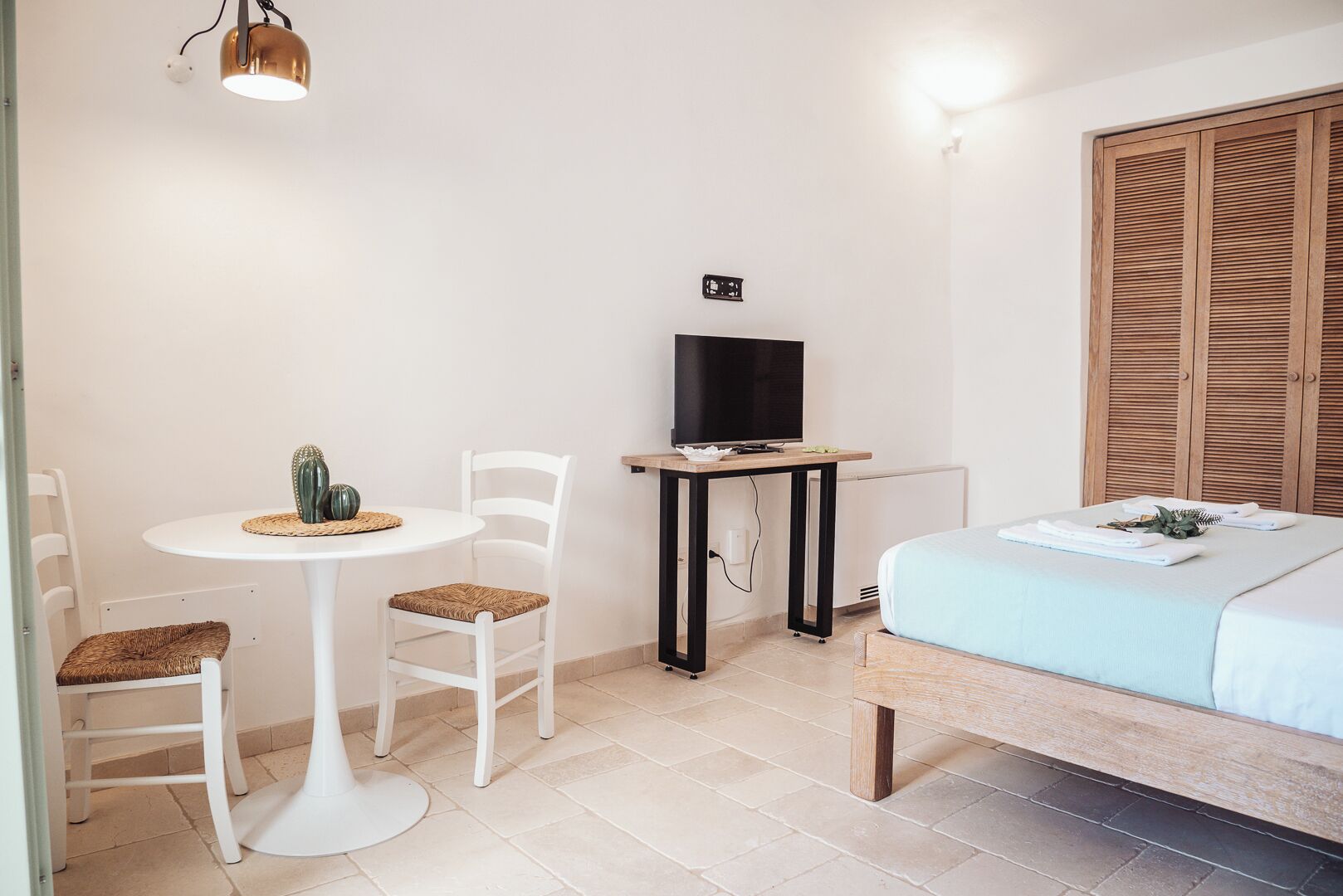Una habitación pequeña con cama, una mesa con sillas, un televisor y un armario de madera.