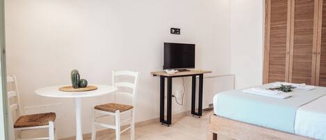 Una habitación pequeña con cama, una mesa con sillas, un televisor y un armario de madera.
