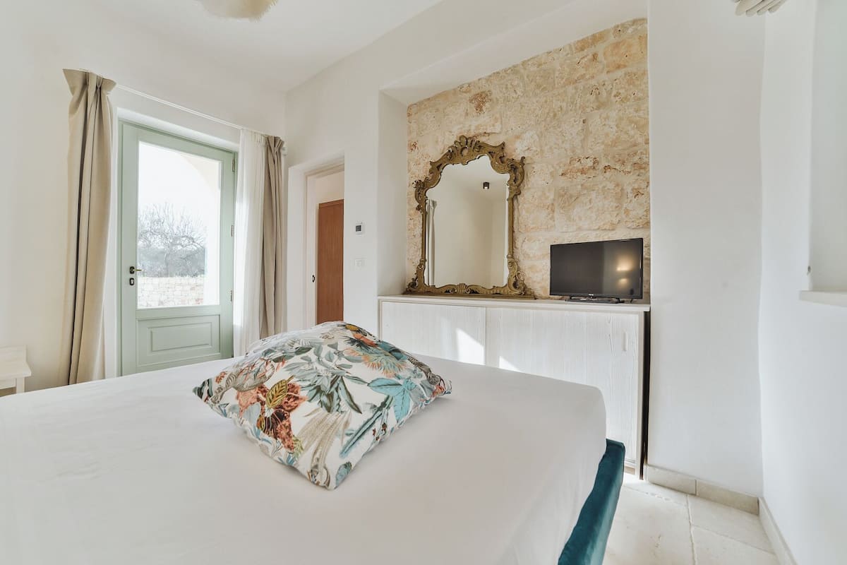 Une chambre à coucher avec un lit, un téléviseur posé sur un meuble, un miroir et une porte donnant sur l’extérieur.