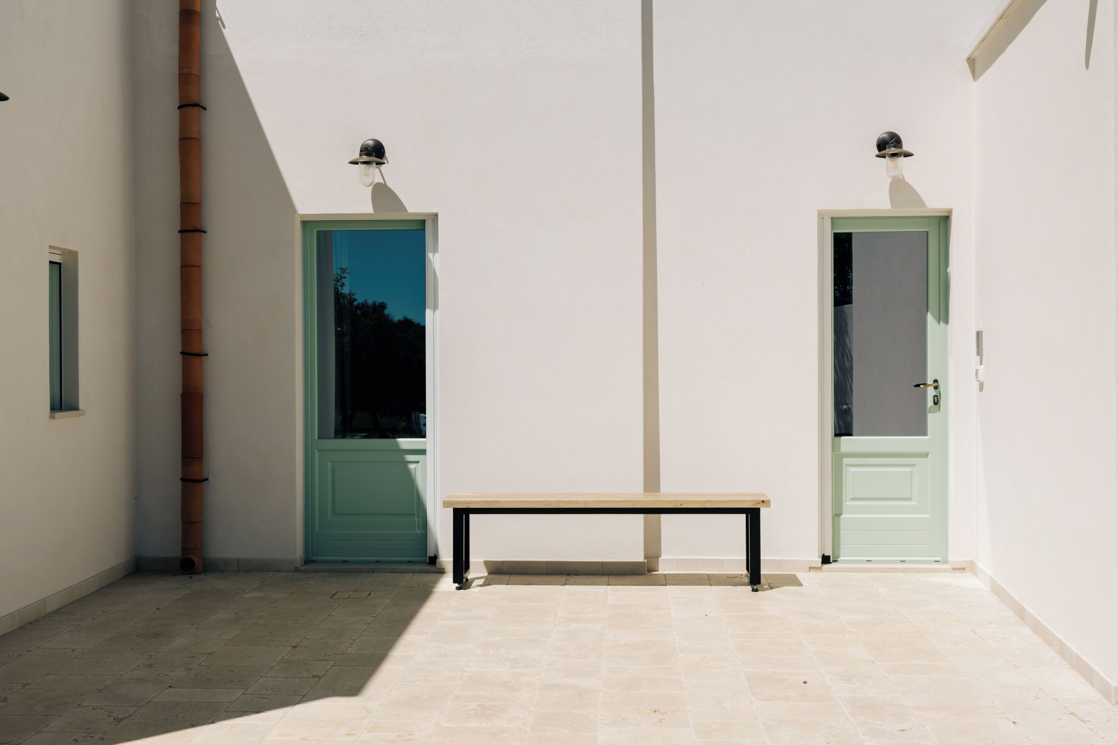 A corridor with a bench, two doors with green frames, and a light fixture on the wall.