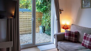 A living room with a sofa, a TV, and a sliding glass door leading to a garden. - The Perk Inn, Cosy & Secluded Garden Lodge (Poole)