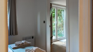 A bedroom with a bed, a radiator, a window, and a door leading to a balcony. - The Perk Inn, Cosy & Secluded Garden Lodge (Poole)