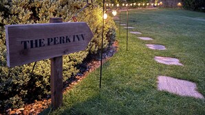 A wooden sign with 'THE PERK INN' written on it, surrounded by well-maintained grass and a stone pathway. - The Perk Inn, Cosy & Secluded Garden Lodge (Poole)
