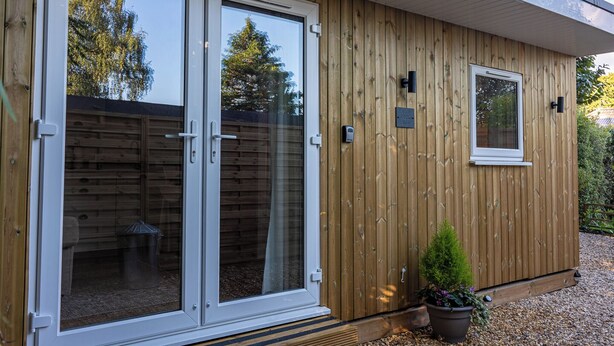 A wooden exterior with a sliding glass door, a small window, and a potted plant. - The Perk Inn, Cosy & Secluded Garden Lodge (Poole)