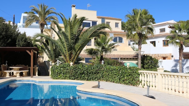 A swimming pool with a pergola, palm trees, and a building with a tiled roof. - Charming finca with pool and large garden in an idyllic setting in Xaló (Teulada)