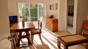 A dining area with a wooden table and chairs, a TV, and a view of a garden through glass doors. - Charming finca with pool and large garden in an idyllic setting in Xaló (Teulada)