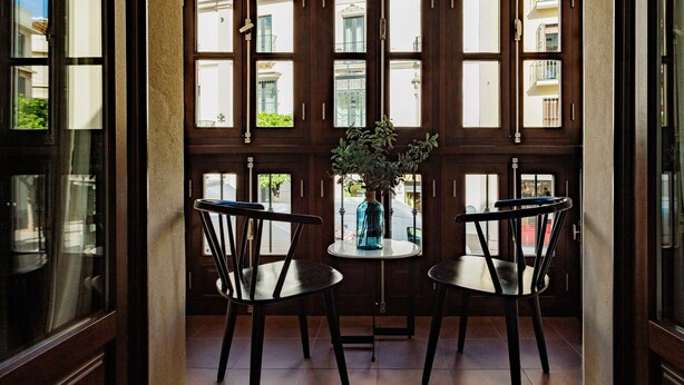 Ein Zimmer mit einem großen Fenster, zwei Stühlen, einem kleinen Tisch und einer Vase mit Pflanzen.