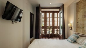 Ein Hotelzimmer mit Bett, Wand-Fernseher, Esstisch mit Stühlen und Blick durch eine offene Tür.