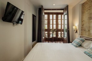 Ein Hotelzimmer mit Bett, Wand-Fernseher, Esstisch mit Stühlen und Blick durch eine offene Tür.