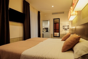 Ein Hotelzimmer mit Bett, Vorhängen, einem an der Wand montierten Fernseher und einem durch eine offene Tür einsehbaren Badezimmer.