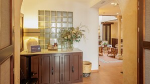 A reception area with a wooden counter, a vase with flowers, a sign, and a tiled floor leading to a seating area. - Cathedral Apartment: Historic Center, Giralda & Pool in Seville (Sevilla)