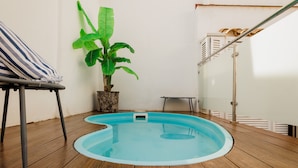 Um deck de madeira com uma piscina pequena, uma cadeira listrada e um vaso de planta.
