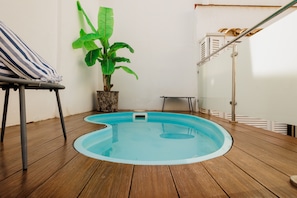 Eine Holzterrasse mit einem kleinen Pool, einem gestreiften Stuhl und einem Topfpflanzen.