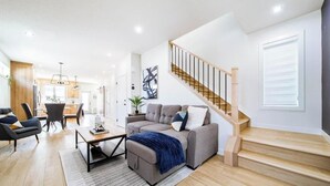Een moderne woonkamer met een bank, salontafel, stoelen, een trap en een eethoek.
