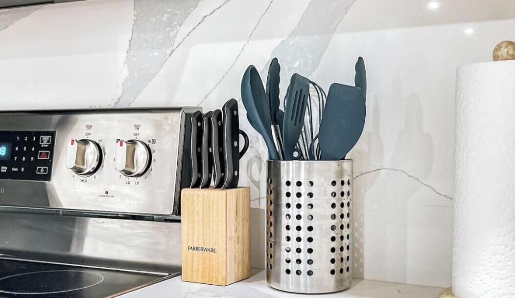 Une cuisine équipée d’une cuisinière, d’un bloc à couteaux de la marque Farberware et d’un porte-ustensiles en métal perforé.