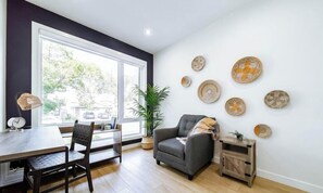 A modern living room with a dining area, large windows, and decorative woven wall art. - Jasper Retreat - AC - Patio - BBQ & Firepit - Near DT/WEM (Edmonton)