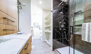 Een moderne badkamer met een marmeren douche, houten kastjes en een wit aanrecht.