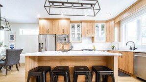 Een moderne keuken met houten kastjes, een roestvrijstalen koelkast, een koffiezetapparaat en een groot eiland met barkrukken.