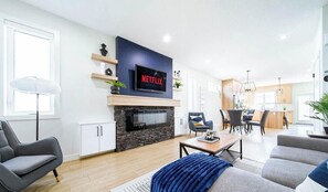 A modern living room with a fireplace, a TV mounted above it, and a dining area in the background. - Jasper Retreat - AC - Patio - BBQ & Firepit - Near DT/WEM (Edmonton)