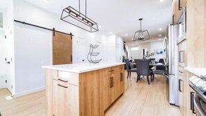 Een moderne keuken met houten kastjes, een centraal eiland, hanglampen en een eethoek met stoelen en een tafel.