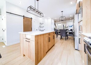 Een moderne keuken met houten kastjes, een centraal eiland en een eethoek met stoelen.