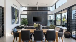 Un espace repas moderne avec une grande table en bois, des chaises noires et un téléviseur à écran plat fixé au mur.