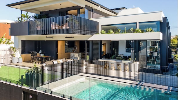 Une maison moderne à deux étages dotée d’une piscine, d’un espace salon extérieur et d’un balcon.