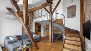 Ein geräumiger Wohnbereich mit Treppe, einer Couch, einem Esstisch und einem Fernseher.