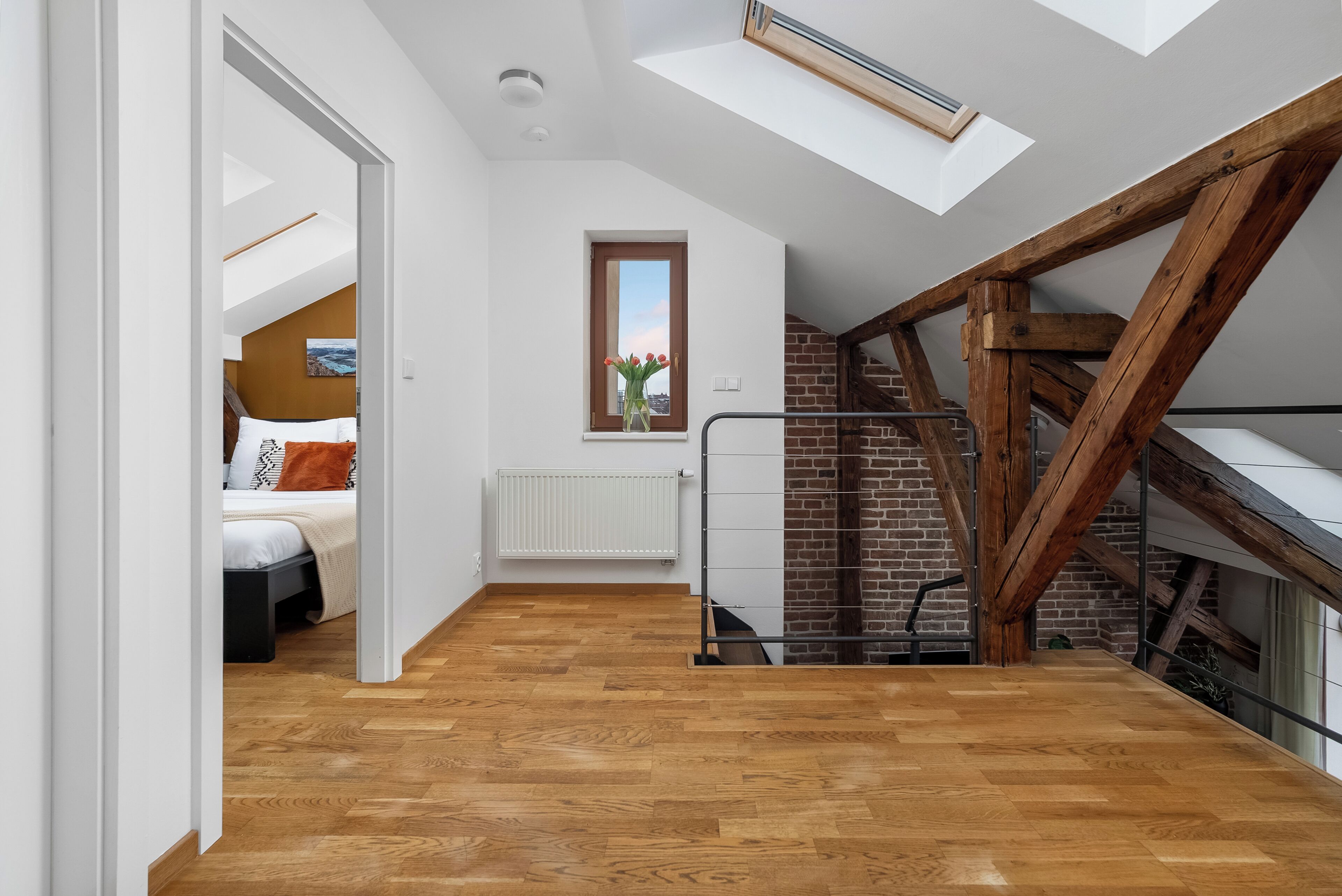 A loft-style bedroom with a skylight, wooden floor, and a brick fireplace.