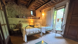 Une chambre rustique avec deux lits en métal, un mur en pierre, une petite fenêtre et un sol carrelé.