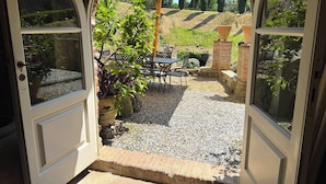Une porte ouverte donnant sur un patio extérieur équipé d’une table, de chaises et d’un grand parasol.