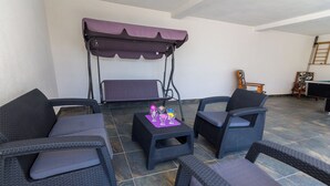 Een overdekt terras met rieten meubels, een schommel en een kleine tafel met drankjes.
