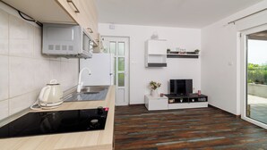 Een moderne keuken met een inbouwmagnetron, fornuis en waterkoker, een zithoekje met televisie, en een schuifpui naar een buitenruimte.