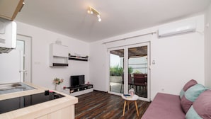 Een moderne keuken met een ingebouwde kookplaat, een eethoek met tafel en stoelen, een bank en een schuifpui naar een terras.
