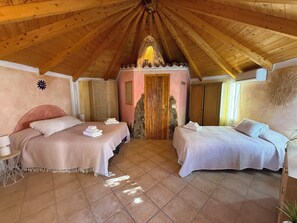 A bedroom with two beds, wooden ceiling beams, a stone wall, and a door with a stone base. - Villa Degli Archi, a beautiful villa with a private pool and the beach just a few meters away   (La Maddalena)