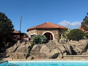 A stone building with a red-tiled roof, a pool, and large rocks in the foreground. - Villa Degli Archi, a beautiful villa with a private pool and the beach just a few meters away   (La Maddalena)