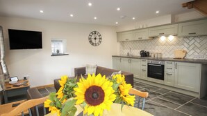 A modern kitchen with light-colored cabinets, a clock, and a dining area with a round table and chairs.