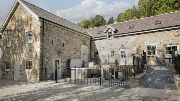 A stone building with a gravel driveway, a metal fence, and a staircase leading to a door.