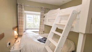 A bunk bed room with a window, curtains, and a bedside table with a lamp.