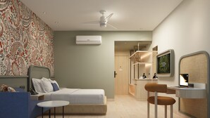 A modern hotel room with a bed, a desk with a computer, a chair, a ceiling fan, and a wall-mounted TV.