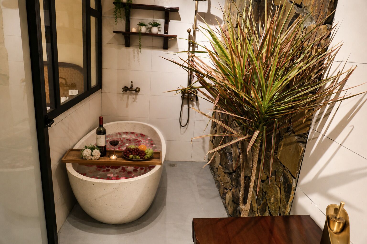 A bathroom with a freestanding bathtub, a wooden shelf with toiletries, and a large plant.