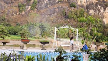 A pool with a metal pergola, potted plants, and a rocky cliff in the background.