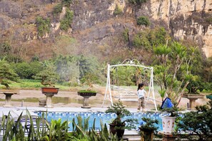 A pool with a metal pergola, potted plants, and a rocky cliff in the background. - Tam Coc AppA House (Nam Hoa Lu)