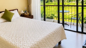 A bedroom with a large bed, a nightstand, a lamp, and a view of a balcony with a table and chairs. - Tam Coc AppA House (Nam Hoa Lu)