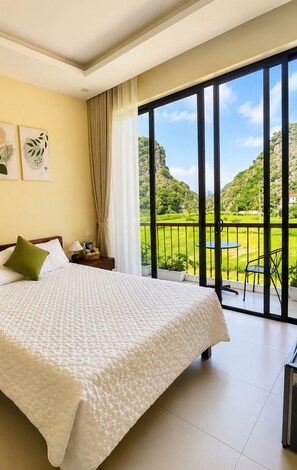 A bedroom with a large bed, a nightstand, a lamp, and a view of a balcony with a table and chairs.