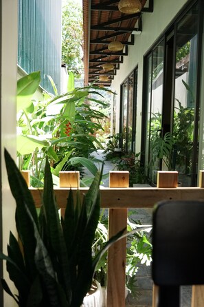 A view through a window with wooden beams, potted plants, and a balcony with a railing.