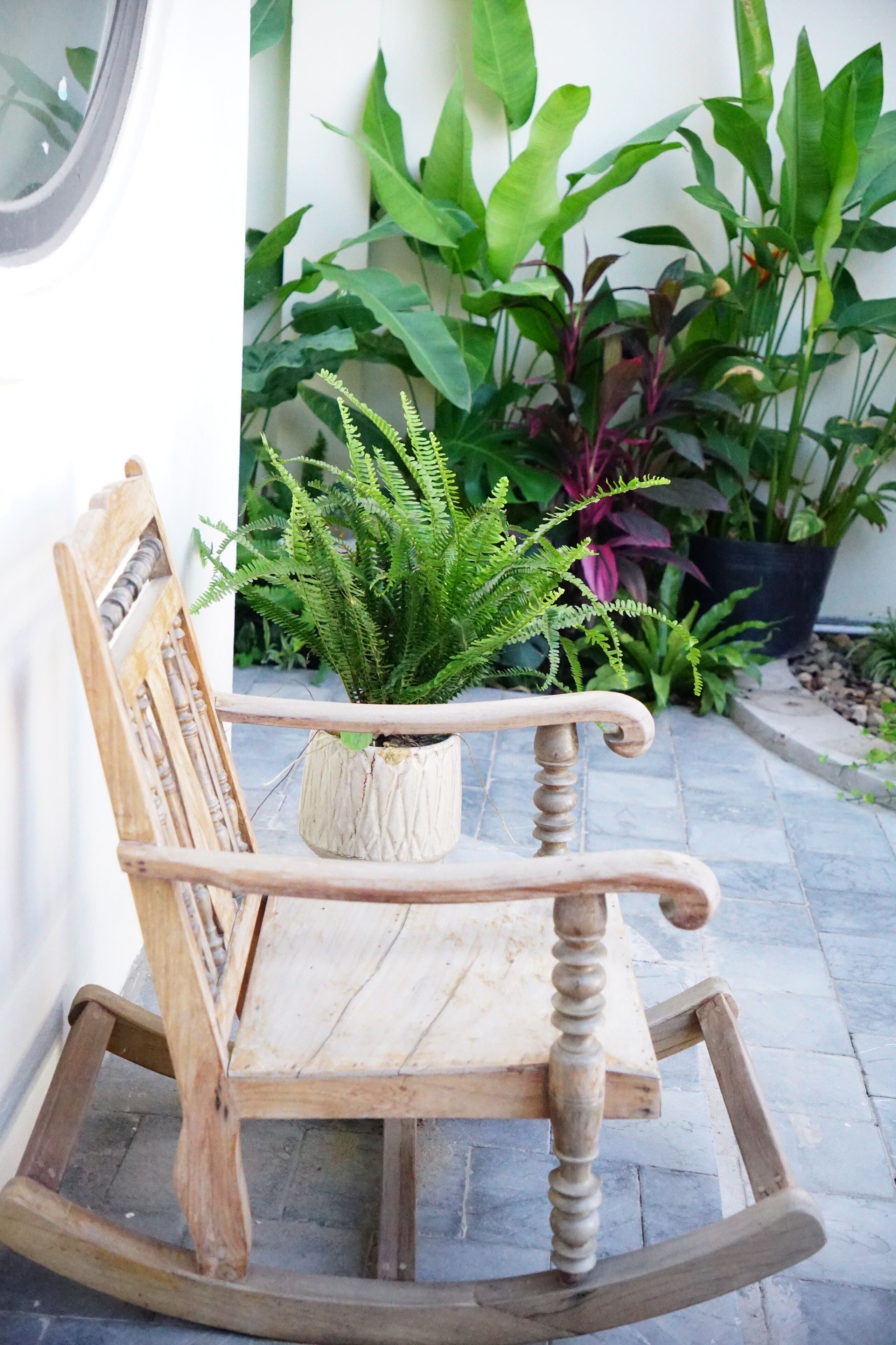 A wooden rocking chair with a potted plant beside it.