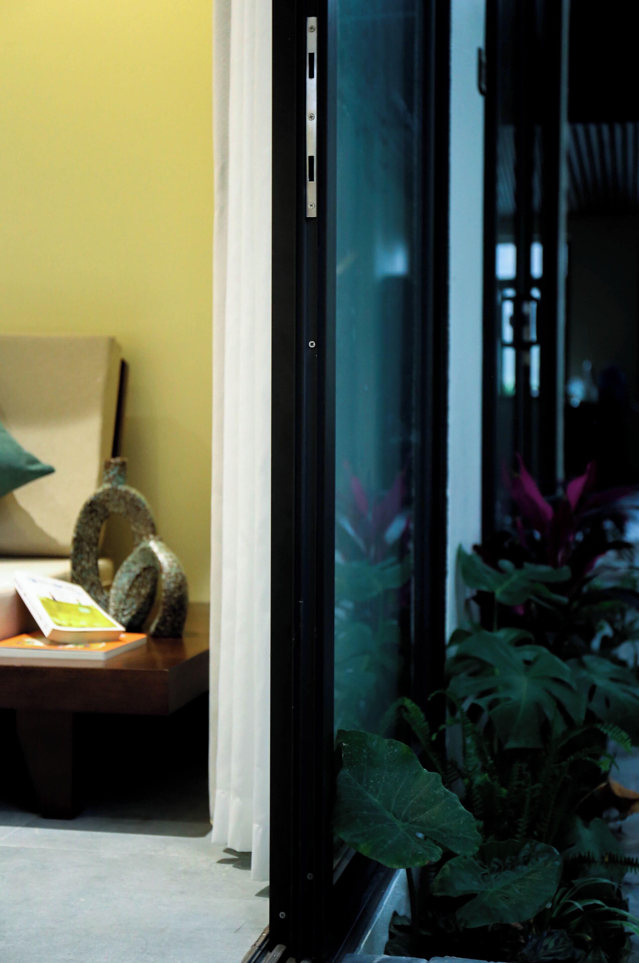 A room with a glass door, a wooden table with a book and a decorative item, and a potted plant.