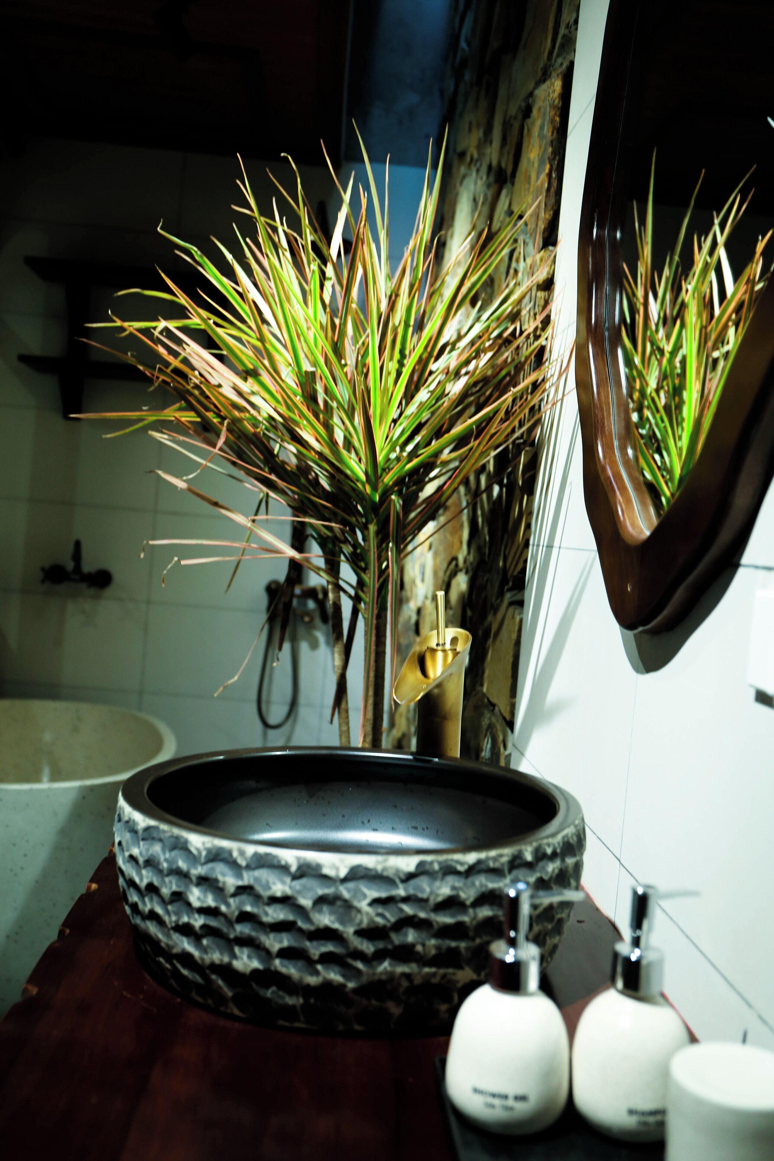 A bathroom with a round sink, a mirror, and a plant.