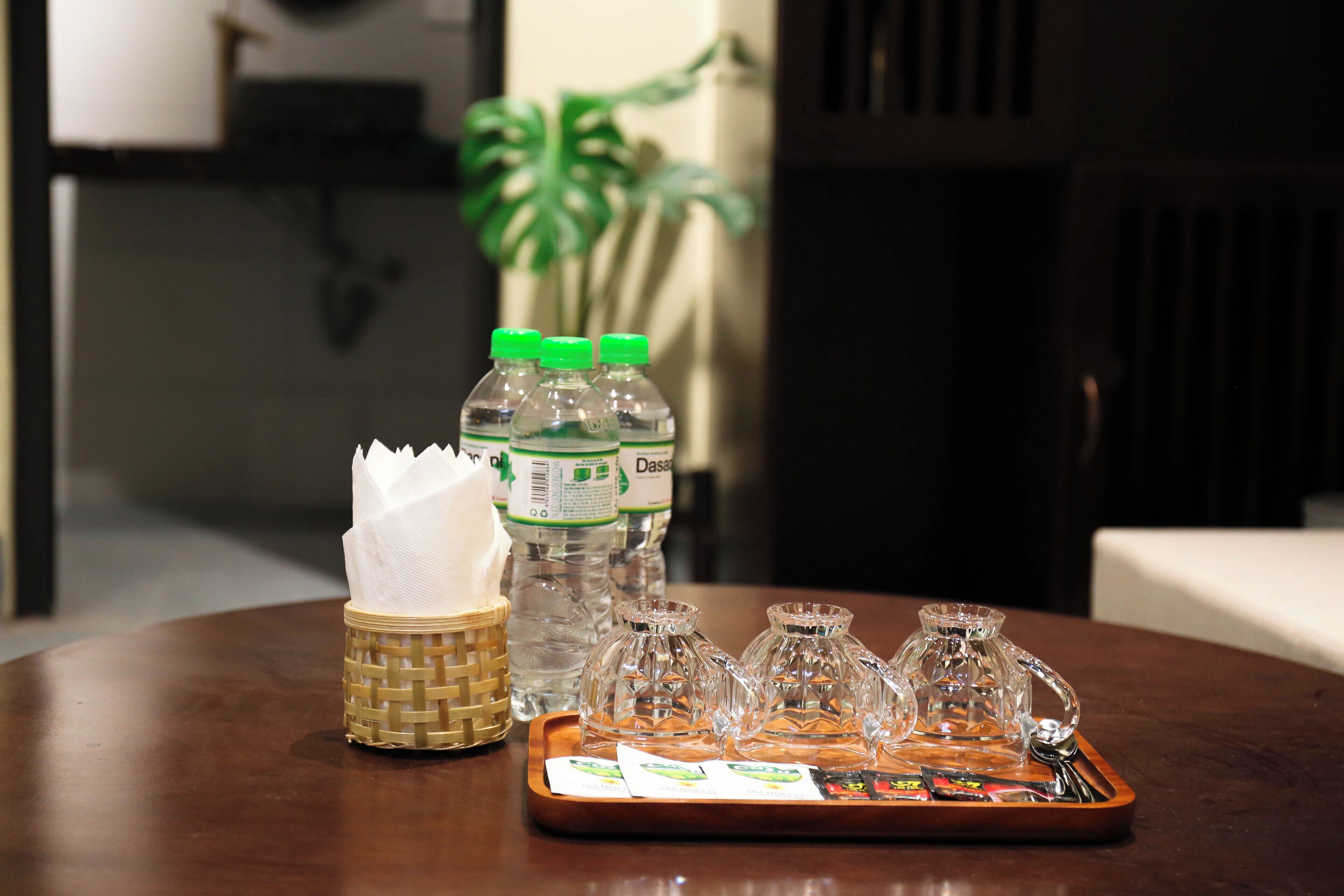 A wooden table with a woven basket, water bottles, and a tray with glassware and napkins.